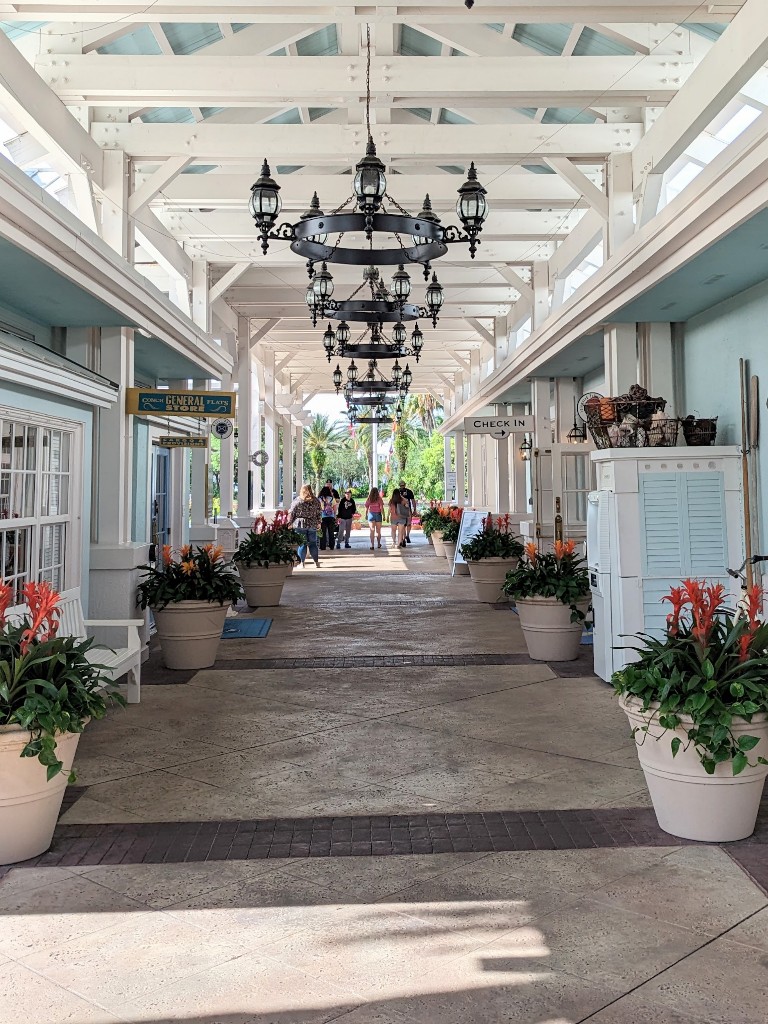 Iron chandeliers hang from white beams on a covered walkway surrounded by pale blue-green buildings at Disney's Old Key West Hospitality House