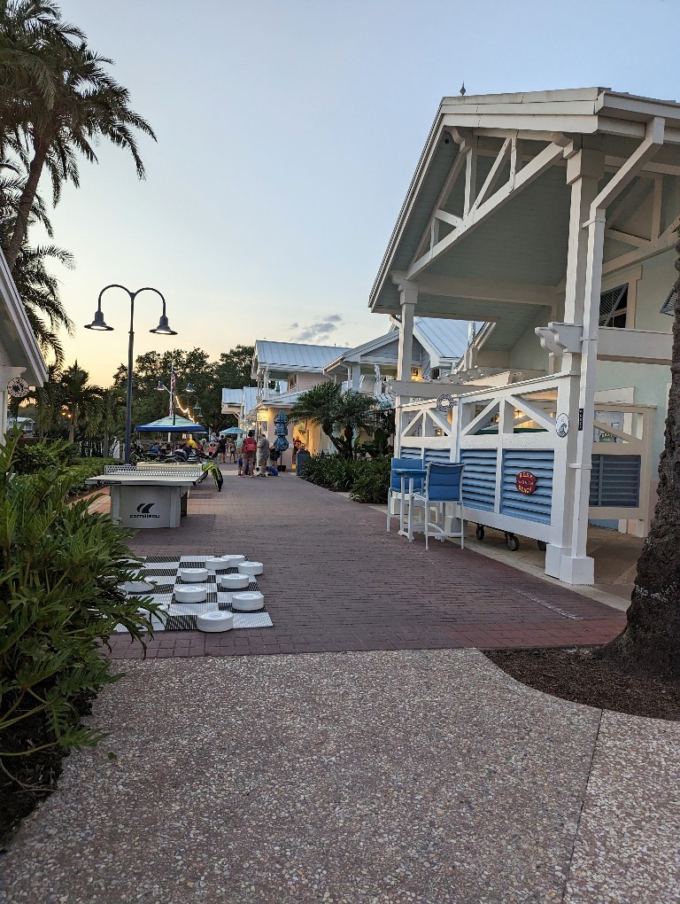 A quaint walkway along the water at Old Key West with a giant checkerboard, tables, and quick service dining