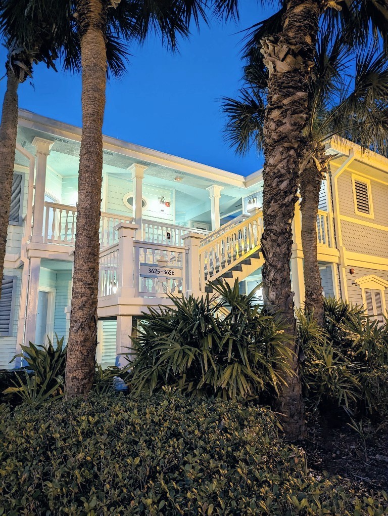 Nighttime view of a two story pale green building surrounded by palm trees at Old Key West