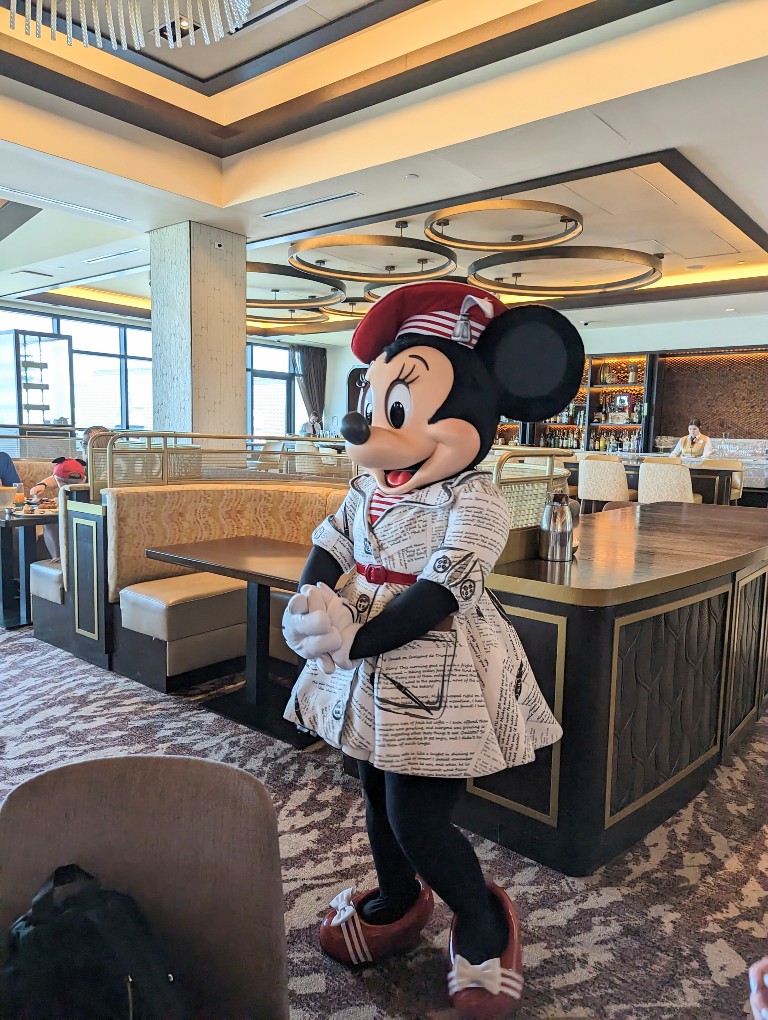 Minnie wears a newsprint inspired dress with bright red beret and belt at Topolino's Terrace