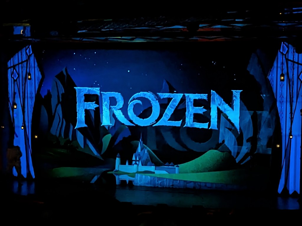 The stage is set for Disney Cruise Line's Broadway style Frozen show with the iconic Frozen title surrounded by a stylized castle and rolling green hills of Arendelle