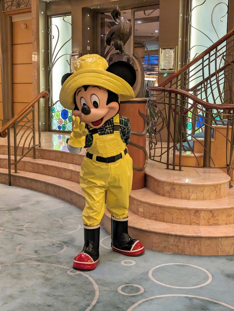 Alaska cruise Mickey dressed in a bright yellow rain hat, gloves, and overalls completes his waterproof look with black and red rainboots