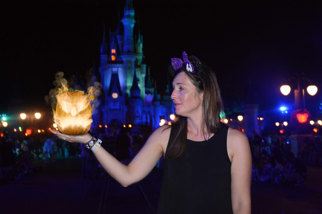 Mickey's Not So Scary Halloween Party photopass option shows a woman looking at a flaming pumpkin in front of Cinderella Castle