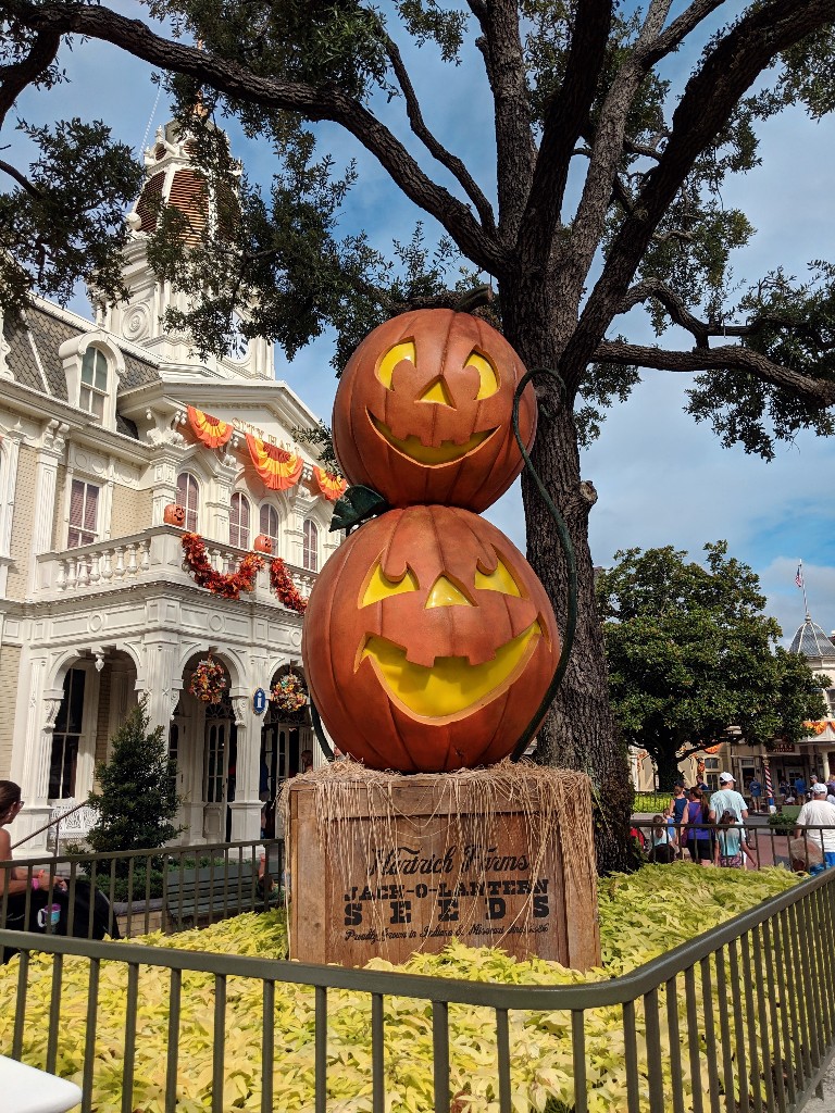 Two jack o'lanterns grin while stacked together on a crate on Main Street USA while town hall is decorated with fall bunting in the background