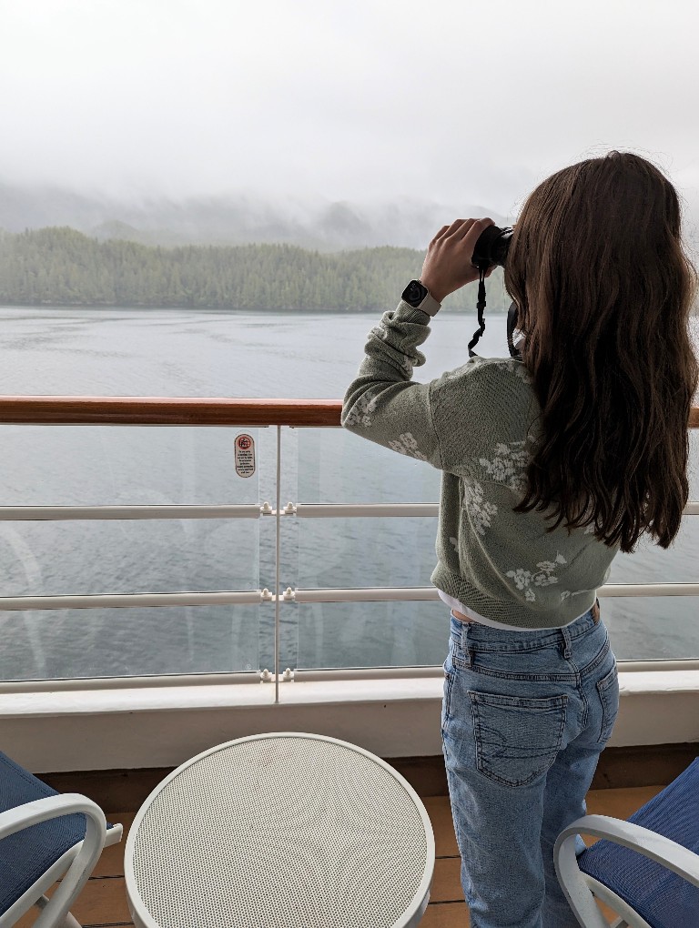 A girl looks along the shore with binoculars while on a Disney Alaska cruise