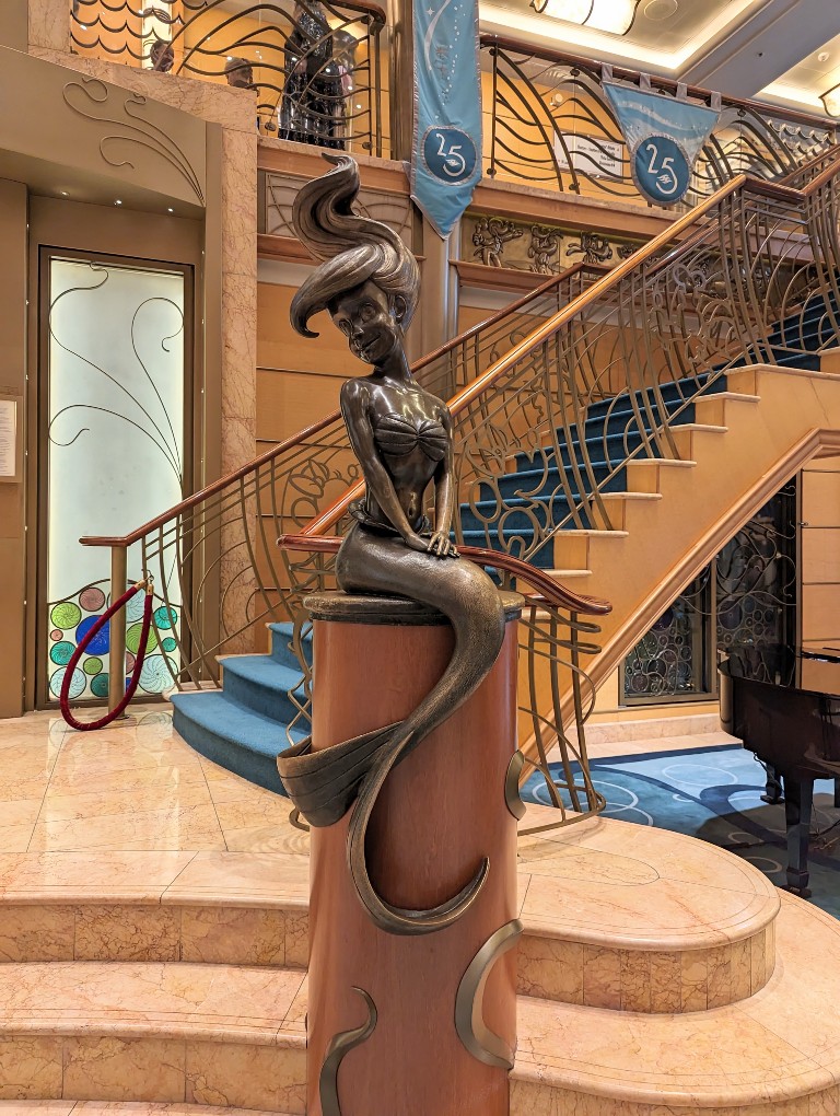 Disney Wonder's lobby with a grand staircase leading up and a bronze Ariel statue make a stunning welcome to Disney Wonder