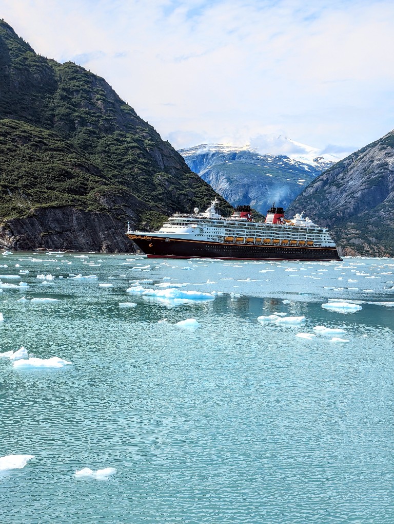 The Disney Wonder cruise ship with mountains in the background and small glaciers surrounding it