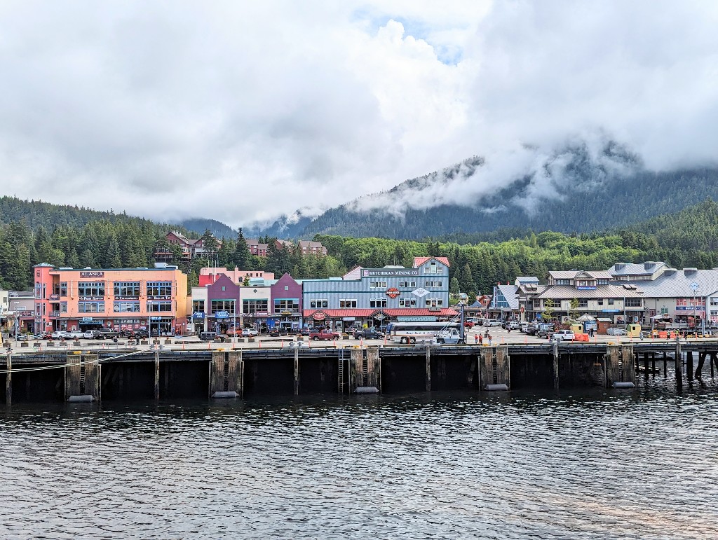 A small town nestled on the edge of water with sweeping views of pine trees behind seen from our Disney Alaska cruise stateroom