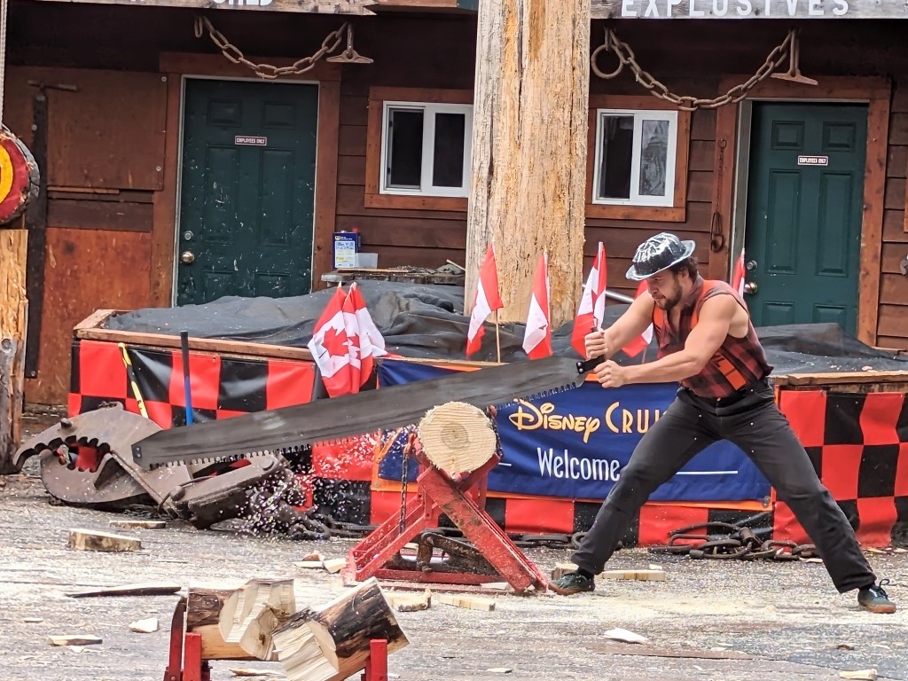 A burly lumberjack in a plaid check shirt saws away at a log during The Great Lumberjack Show on a Disney Alaska cruise port adventure