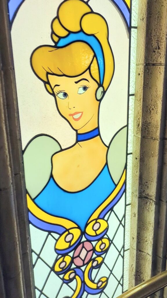 A stained glass window with an image of animated Cinderella in her blue dress on the way up the spiral staircase at Cinderella's Royal Table