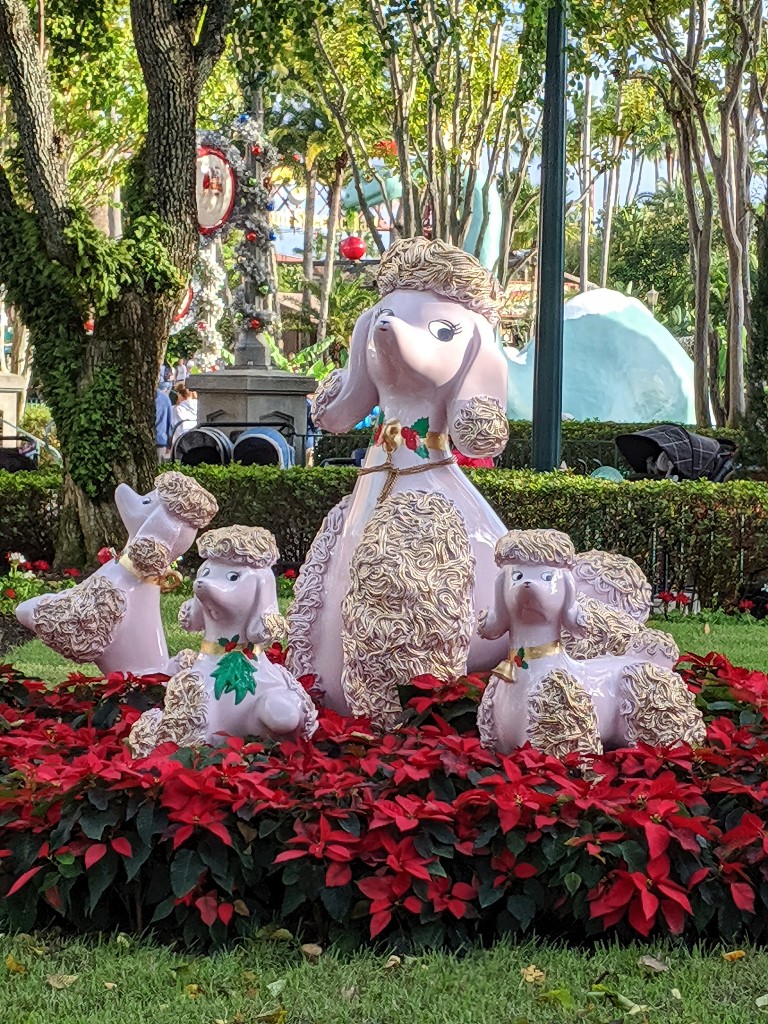 A large porcelain inspired poodle and her puppies are surrounded by bright red poinsettias at Hollywood Studios