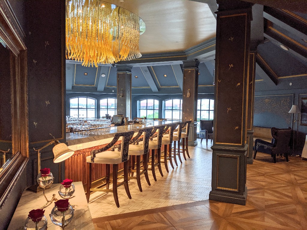 Dark blue walls, rich wood, and a stunning gold chandelier are an elegant interpretation of Beauty and the Beast at Enchanted Rose bar at Grand Floridian