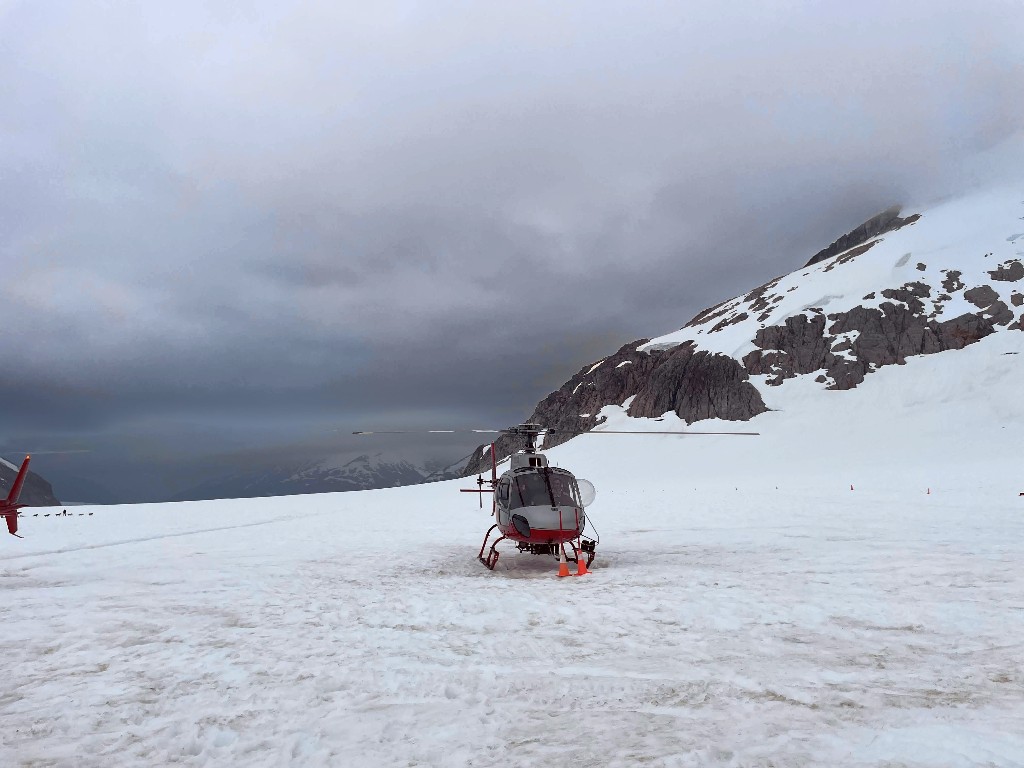 A dark sky and clouds behind a helicopter landing on Mendenhall Glacier at the dog sled camp
