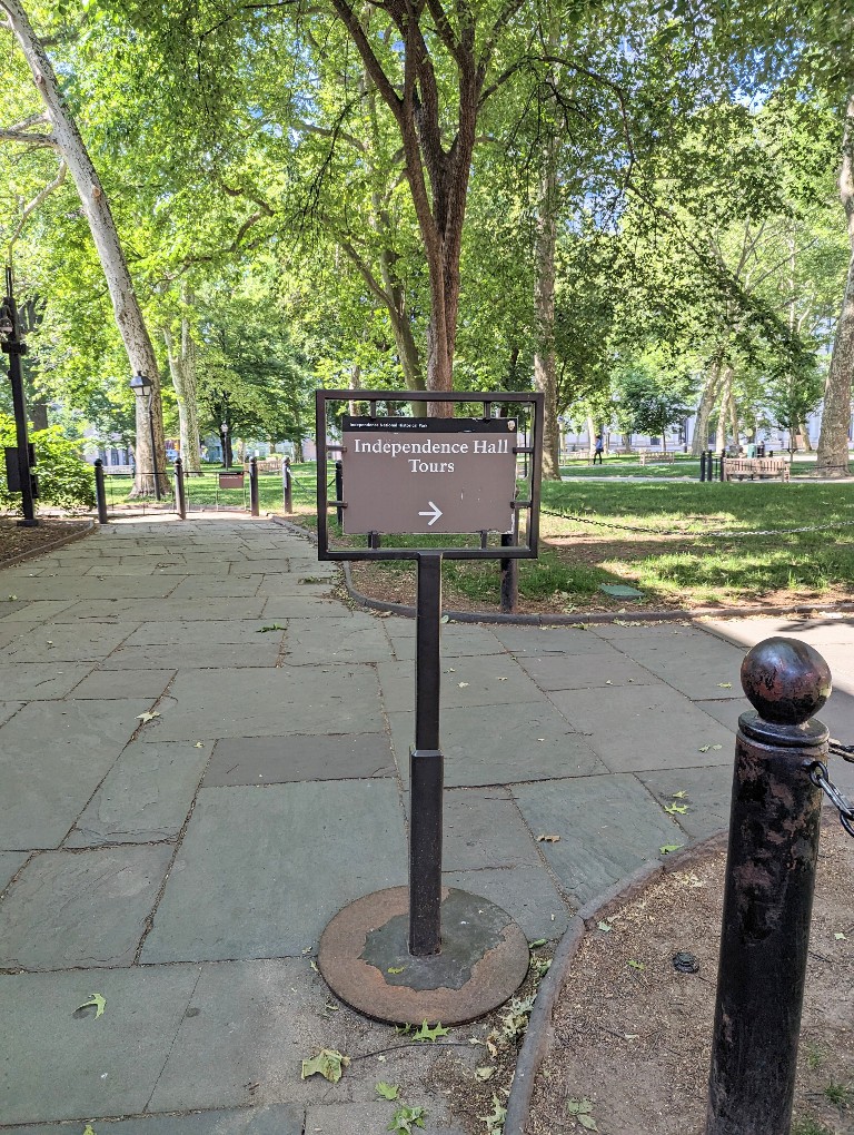 A National Parks sign along a pathway directs visitors where to find meeting area for Independence Hall guided tours