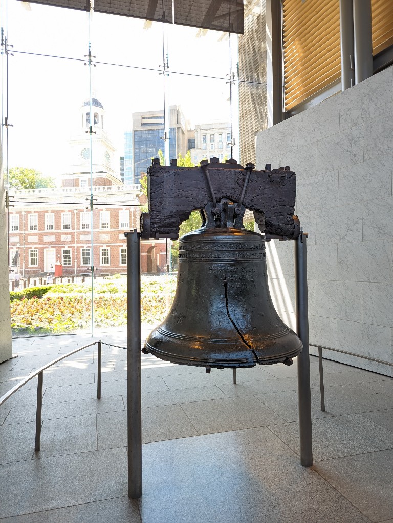 Close up view of Liberty Bell with her iconic crack and Independence Hall in the background