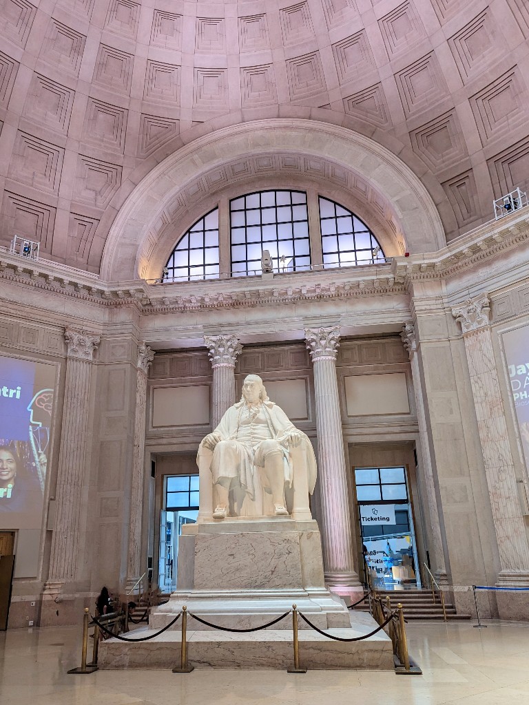 A large statue of Benjamin Franklin seated upon a chair looms in the high ceiling entrance of The Franklin Institute in Philadelphia