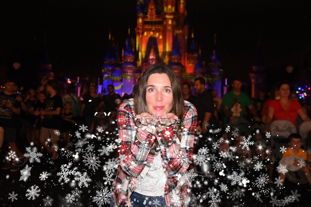 A woman blows "snowflakes" off of her hands in a special Mickey's Very Merry Christmas PhotoPass op in front of Cinderella Castle