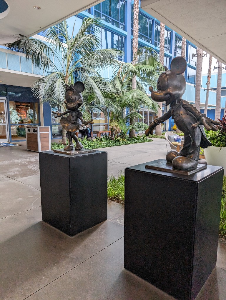 Bronze statues of Mickey and Minnie Mouse in front of palm trees at the entrance of Disneyland Hotel