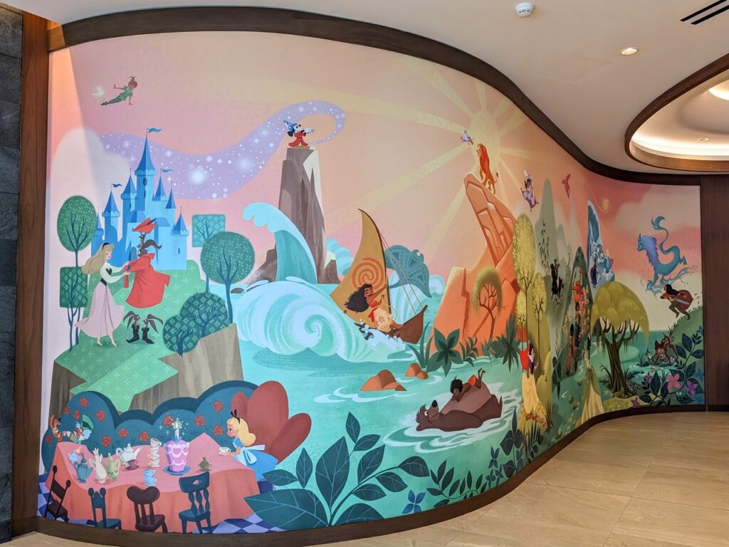 A large mural in the Disneyland Hotel villa tower lobby with a collection of scenes and characters blended together. For example, Aladdin and Jasmine fly on a magic carpet over Merida riding a horse.