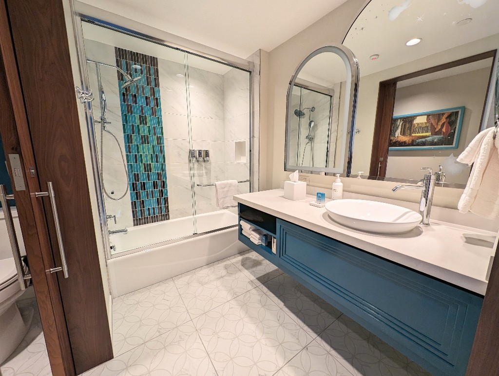 A gray and white tiled shower with a blue-green mosaic is a focal point in the Disneyland Hotel studio villa split bathroom