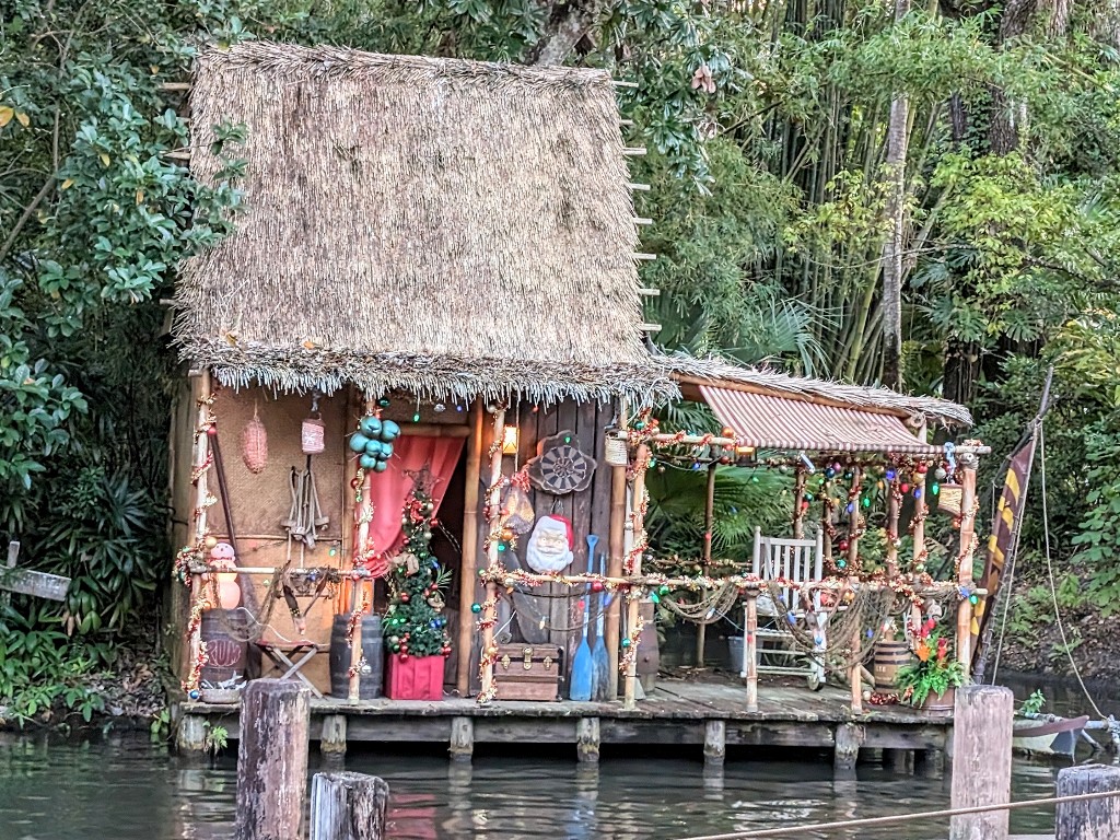 A hut decorated with lights, a Santa wall decoration, and a small Christmas tree is visible across from the Jingle Cruise loading dock