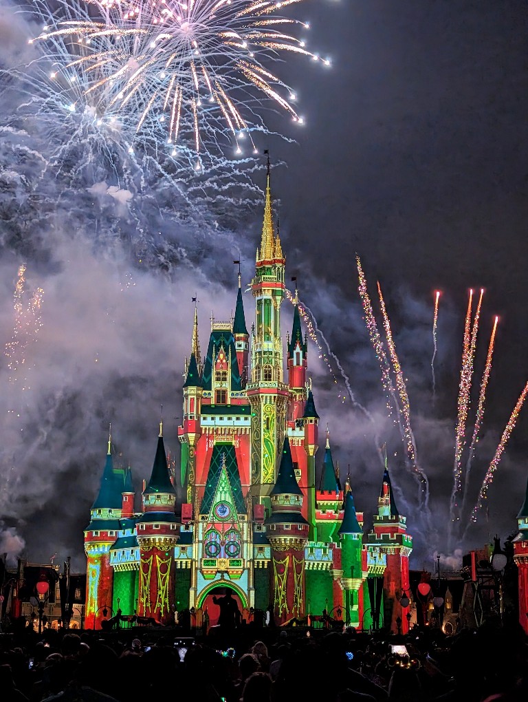 Fireworks explode above a green, red, and gold Cinderella Castle during Minnie's Wonderful Christmastime fireworks at Mickey's Very Merry Christmas Party