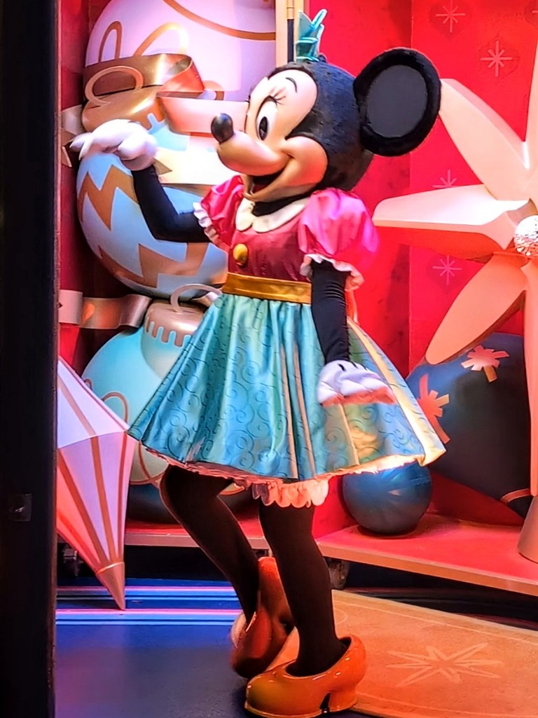 Minnie wearing a pink top and full mint green skirt waves to guests at Disney Jollywood Nights