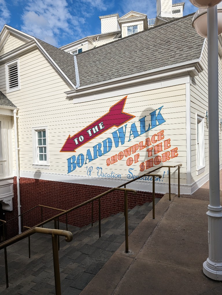 A sign pointing down a set of stairs says "To The BoardWalk showplace of the shore"