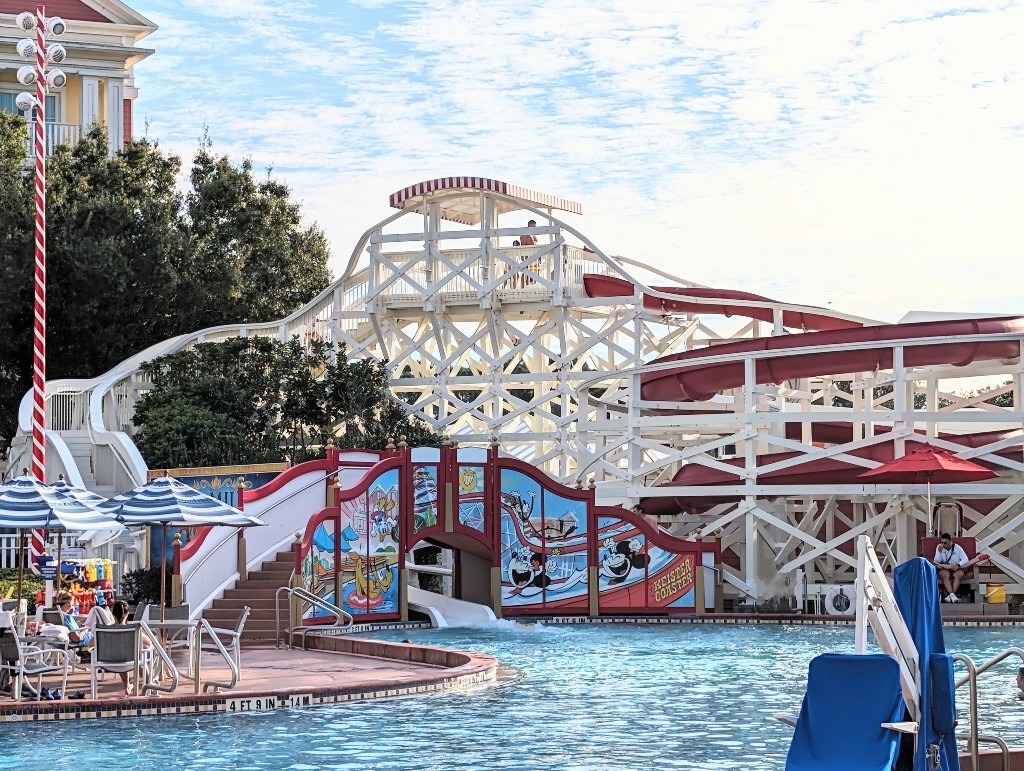 A wooden roller coaster inspired water slide flows into a blue bottomed pool at Disney's Boardwalk Inn and Villas