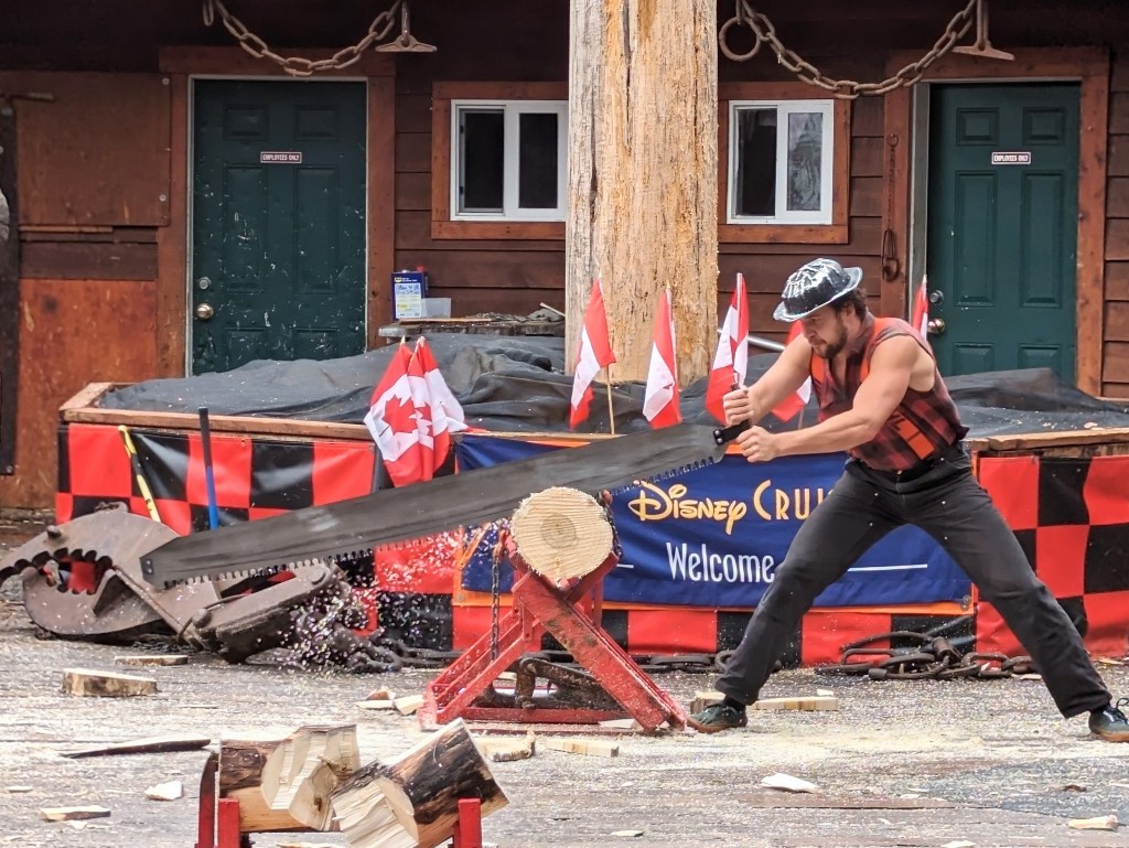 A lumberjack in a red and black checkered shirt uses a long saw to quickly carve through a log