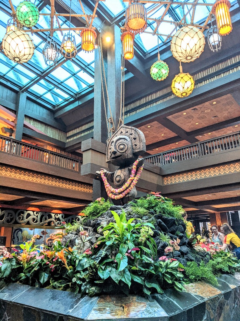 A wooden figure draped in a colorful lei and surrounded by tropical plants welcomes guests to Disney's Polynesian Village Resort