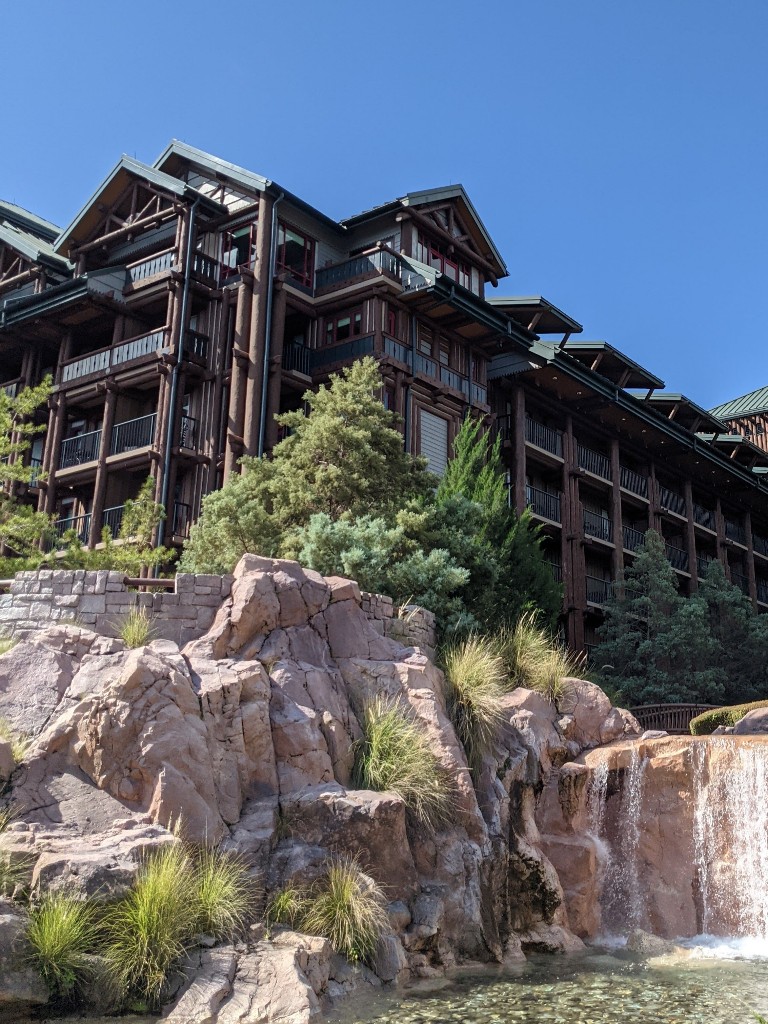 Rocky outcroppings covered in pine trees with a cascading waterfall provide ambiance for the green roofed, log cabin styling of Disney's Wilderness Lodge