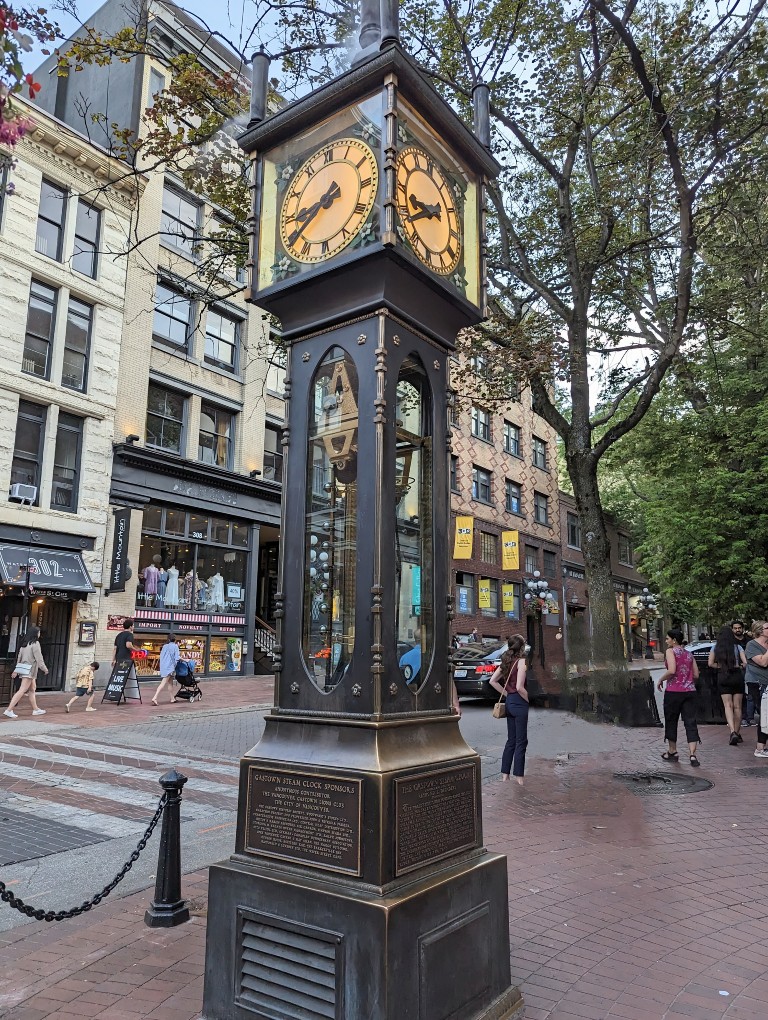 The Gastown Steam Clock in the foreground with shops and people walking along the sidewalk in the background