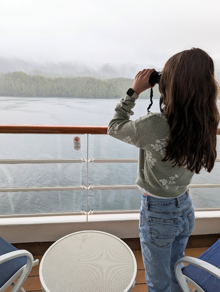 A teen girl uses binoculars to look out over the shores during a Disney Alaska Cruise