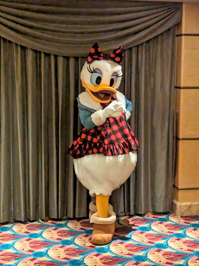 Daisy Duck meets guests in a red and black buffalo check plaid dress, sherpa lined boots, and a jacket