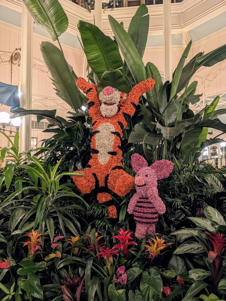 Tigger and Piglet topiaries in bright colors stand out in the deep green background at the entrance of The Crystal Palace